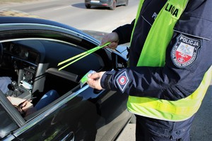 Na zdjęciu widać umundurowanego policjanta, który przekazuje odblaski kobiecie siedzącej w samochodzi