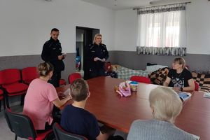 przy stole siedzą kobiety i dziecko a w tle umundurowani policjanci