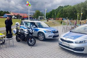 z lewej strony policjant stoi obok motocykla i radiowozów