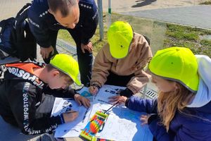 troje dzieci przy stoliku malują, obok stoi policjant