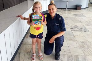 policjantka obok dziewczynki trzymającej ulotkę bezpieczne wakacje