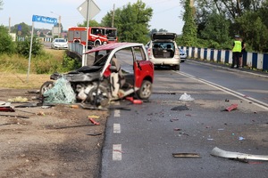 na drodze rozbity pojazd typu microcar, z prawej strony policjant, w tle radiowóz i wóz strażacki