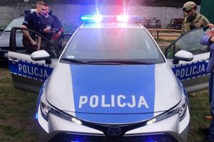 z lewej strony policjant stoi obok otwartego radiowozu