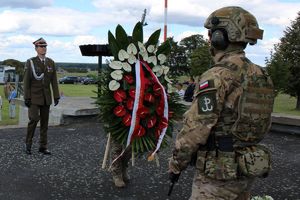 żołnierz w stroju galowym, przed nim wieniec białoczerwonych kwiatów