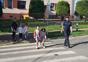 dzieci przechodzące przez jezdnię na pasach obok policjantka