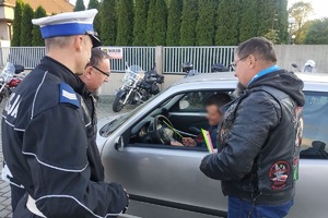 Policjant wspólnie z członkiem klubu motocyklowego wręczają odblaski i ulotki kierowcy samochodu