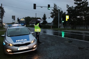 policjant stoi obok radiowozu i mierzy radarem prędkość nadjeżdżającego pojazdu