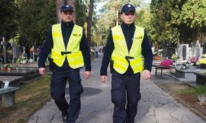 Dwóch policjantów idzie alejką między nagrobkami.