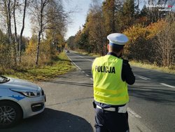 Umundurowany policjant ruchu drogowego dokonujący pomiaru prędkości nadjeżdżającego pojazdu.