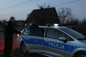 Na zdjęciu widzimy radiowóz oraz policjanta, który otwiera tylne drzwi radiowozu. Z radiowozy wychodzi mężczyzna.