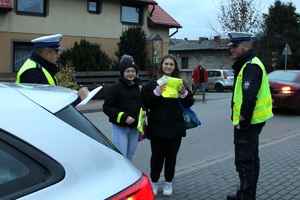 Zdjęcie przedstawia dwóch umundurowanych policjantów oraz dwie piesze, które prezentują otrzymane elementy odblaskowe.