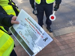 Zdjęcie przedstawia fragmenty sylwetek umundurowanych policjantów oraz plakat Światowego Dnia Pamięci Ofiar Wypadków Drogowych