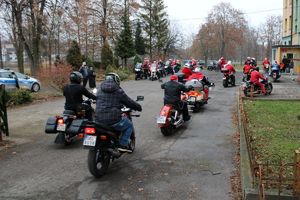 Zdjęcie przedstawia motocyklistów w przebraniach Mikołaja wjeżdżających na plac domu dziecka.