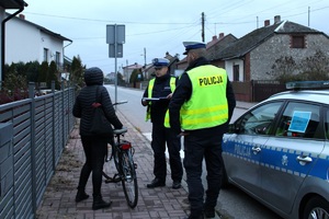 Zdjęcie przedstawia dwóch umundurowanych policjantów rozmawiających z rowerzystką.