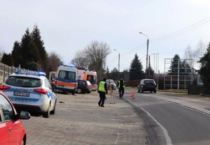 Zdjęcie przedstawia radiowóz stojący na poboczu oraz policjantów wykonujących czynności na miejscu zdarzenia.