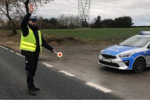 umundurowany policjant wydaje polecenie do zatrzymania pojazdu, w ręce trzyma tarczę do zatrzymywania pojazdu