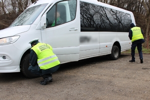 policjant i funkcjonariusz inspekcji transportu drogowego sprawdzają bieżnik opony w busie