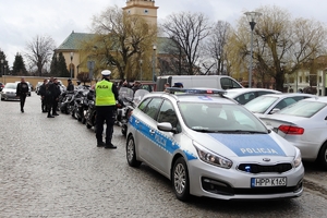 Zdjęcie przedstawia policyjny radiowóz, policjanta oraz motocyklistów.