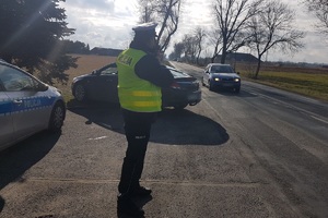 Policjant mierzy prędkość przejeżdżającemu samochodowi.