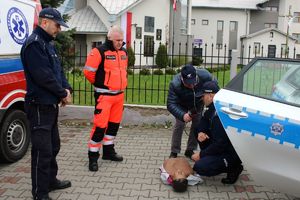 Zdjęcie przedstawia policjantów, ratownika medycznego oraz dziennikarza, któremu jeden z policjantów prezentuje na fantomie jak prawidłowo udzielić pierwszą pomoc.