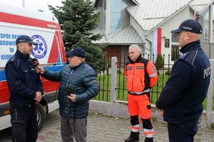 Zdjęcie przedstawia policjantów, z których jeden udziela wywiadu dziennikarzowi oraz ratownika medycznego.