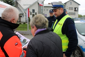 Zdjęcie przedstawia ratownika medycznego prezentującego kierującej zdjęcia ze śmiertelnych wypadków drogowych oraz policjanta.