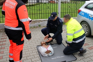 Zdjęcie przedstawia policjanta, który prezentuje kierowcy jak prawidłowo wykonać resuscytację krążeniowo-oddechową.