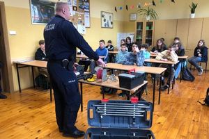 Dzielnicowy prezentuje uczniom sprzęt policyjnych pirotechników.