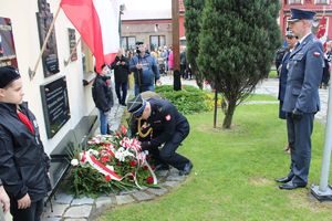 Na zdjęciu widać uczestników strażak ubrany w mundur galowy składa wiązankę kwiatów przy miejscu pamięci narodowej