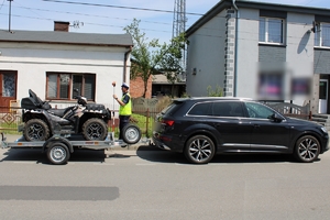 Zdjęcie przedstawia pojazd z podpiętą przyczepą, na której znajduje się quad oraz policjanta robiącego pomiary.