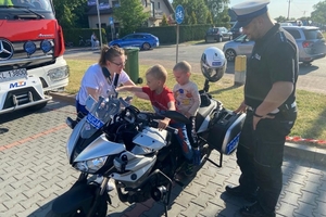 Zdjęcie przedstawia policjanta ruchu drogowego, policyjny radiowóz oraz dzieci.