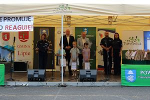 Zdjęcie przedstawia namiot ze sceną, na której znajduje się grupa dzieci oraz, Pani Komendant, Naczelnik Prewencji, Burmistrz Kłobucka, Wójt Gminy Wręczyca Wielka oraz przemawiająca policjantka.