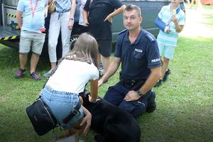 Zdjęcie przedstawia policjanta, psa oraz dziewczynkę głaszcząca psa.