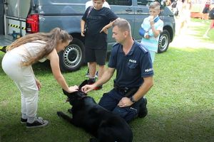Zdjęcie przedstawia policjanta, psa oraz dziewczynkę głaszczącą psa.