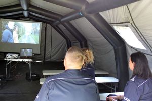 Zdjęcie przedstawia policjantów oglądających film pod namiotem.