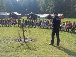 Zdjęcie przedstawia policjanta oraz siedzące na trawie dzieci.