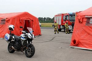 Zdjęcie przedstawia policyjny motocykl oraz namioty ratownicze.