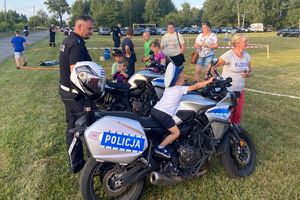 Policjant, policyjny motocykl i dzieci, którym dorośli robią pamiątkowe zdjęcie.