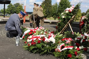 policjant składa wiązankę kwiatów pod pomnikiem