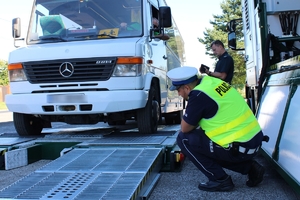 biały bus przechodzi badanie techniczne na mobilnej stacji kontroli, obok znajduje się umundurowany policjant