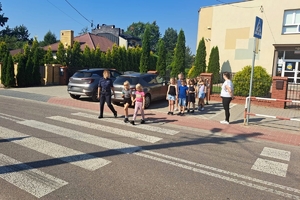 Zdjęcie przedstawia policjantkę oraz dzieci przechodzące przez oznakowane przejście dla pieszych.