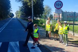 Zdjęcie przedstawia policjantkę oraz dzieci podczas przejścia przez oznakowane przejście dla pieszych.