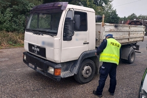 Zdjęcie przedstawia policjanta kontrolującego pojazd ciężarowy.