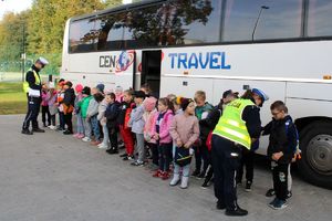 Zdjęcie przedstawia policjantów rozdających odblaski dzieciom stojącym przed autokarem.