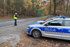 Zdjęcie przedstawia policjanta mierzącego prędkość nadjeżdżającym pojazdom oraz radiowóz.