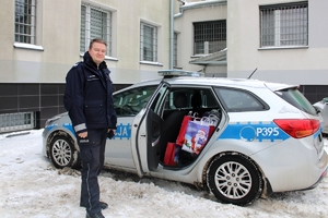 Zdjęcie przedstawia policjanta stojącego obok radiowozu. Drzwi radiowozu są otwarte a wewnątrz znajdują się paczki prezentowe.