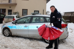 Zdjęcie przedstawia policjanta trzymającego paczki prezentowe. Policjant stoi obok radiowozu.