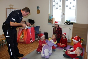 Zdjęcie przedstawia policjanta przekazującego prezenty dzieciom siedzącym obok na dywanie.
