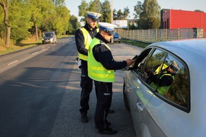 Zdjęcie przedstawia dwóch policjantów drogówki badających trzeźwość zatrzymanego do kontroli kierowcy.