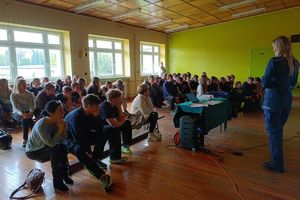 Zdjęcie przedstawia policjantkę w sali, mówiącą do siedzących przed nią dzieci.